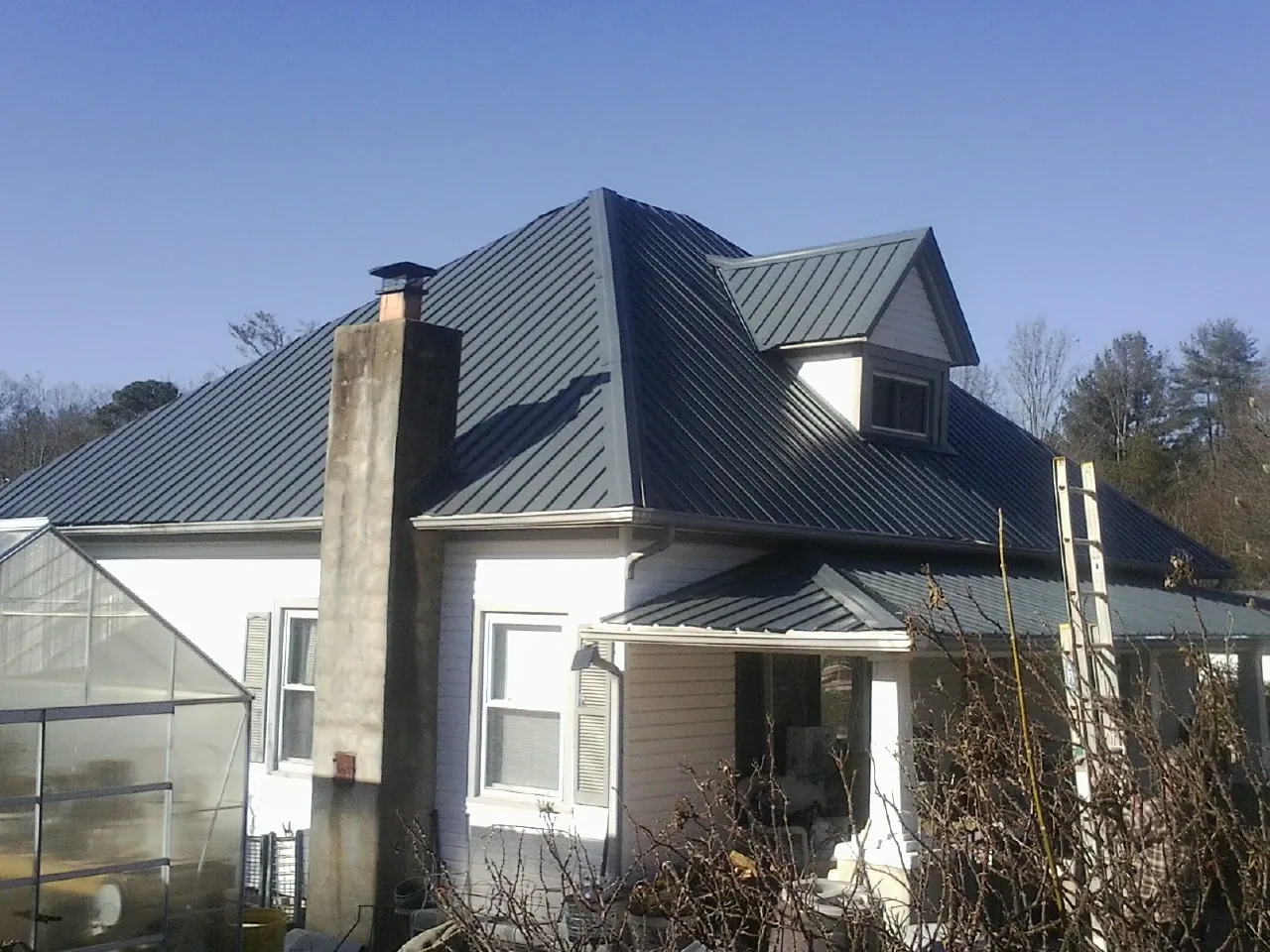 Dark blue standing seam metal roof on a white farmhouse with dormer — Slate & Tile Roof Repair by Roofing Brothers in Maryland Line
