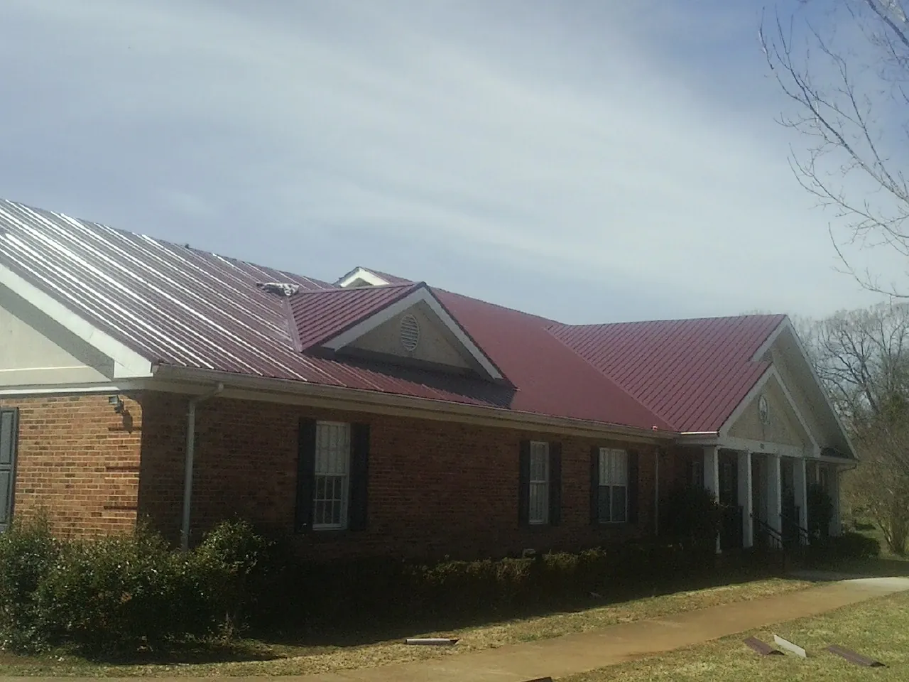 Red metal roof with gabled entries on a long brick building, from a Hail Damage Roof Repair job in Maryland Line