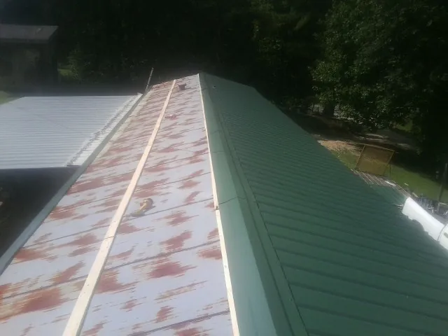 Old rusted panels beside newly installed green metal roofing — Wind Damage Roof Repair by Roofing Brothers in Maryland Line