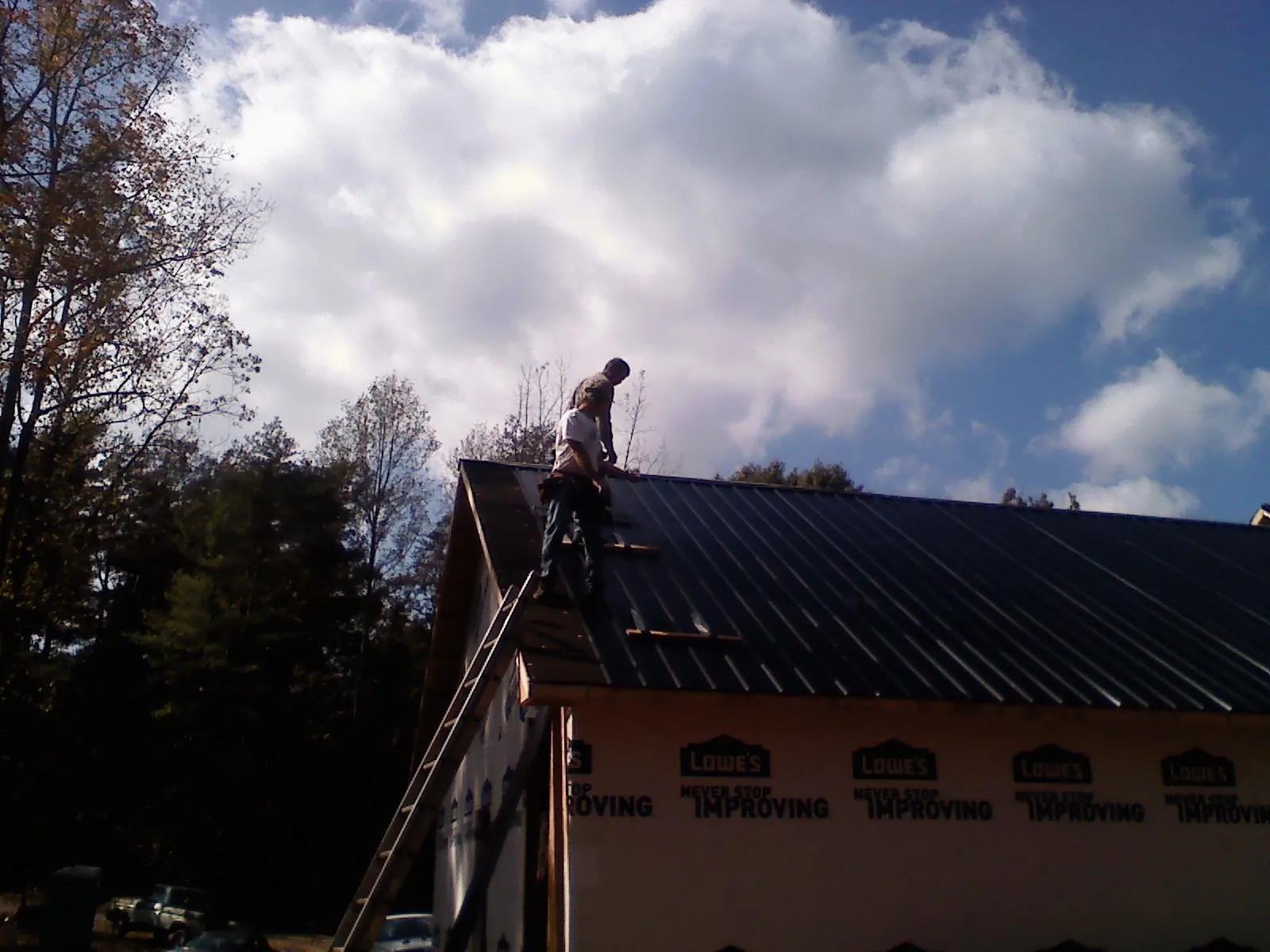 Roofer fastening dark metal panels high against a cloudy sky, from a Roof Inspection job in Maryland Line