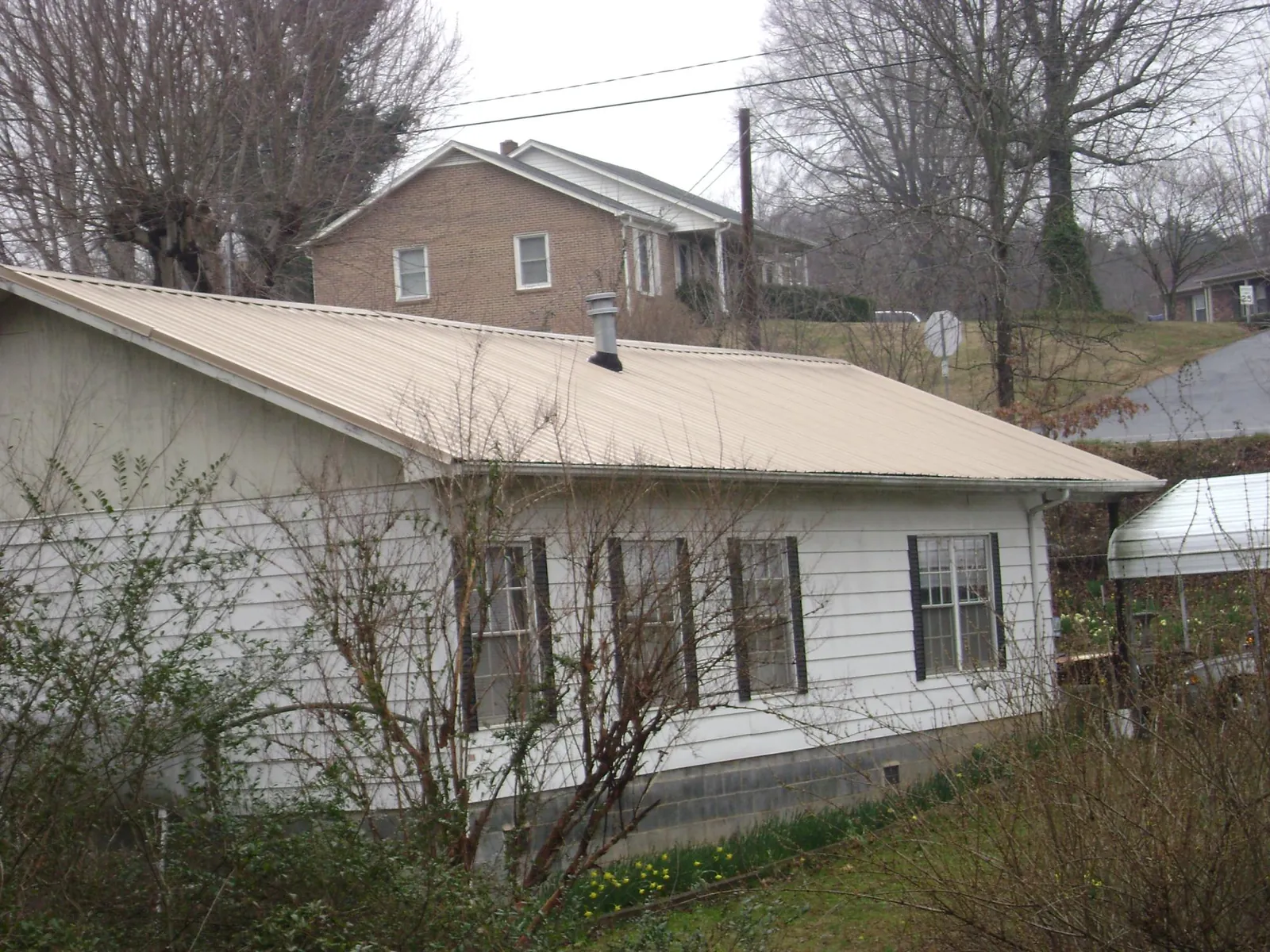 Tan metal roof on a white sided house set into a hillside — Commercial Roofing by Roofing Brothers in Maryland Line